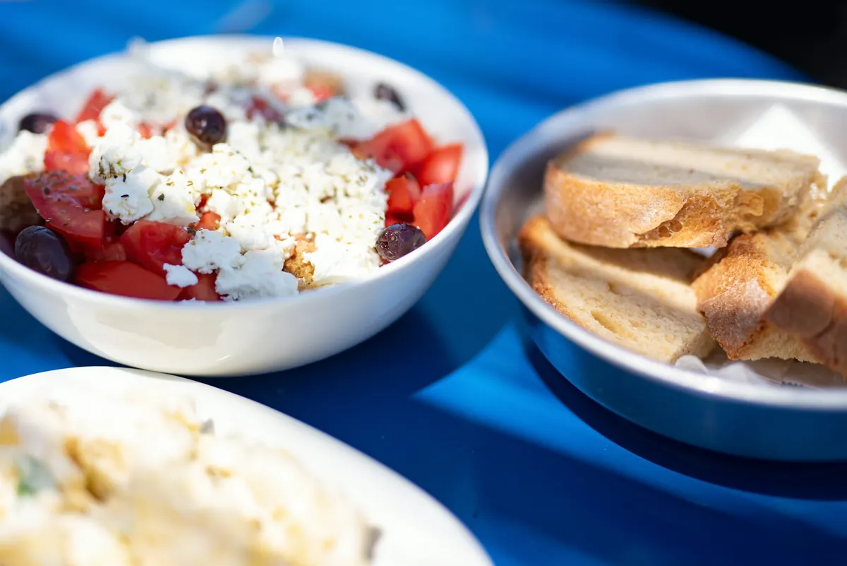 Schalen mit griechischem Salat und Brot auf einem blauen Tisch